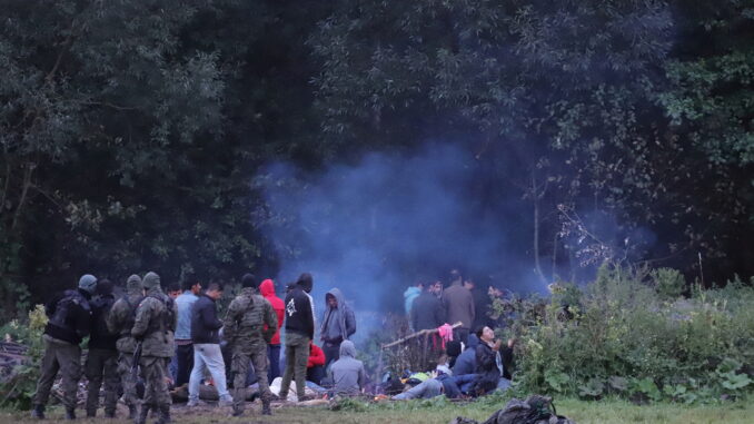 Polish border patrol officers guard a group of migrants who attempted to cross the border between Belarus and Poland near the village of Usnarz Gorny